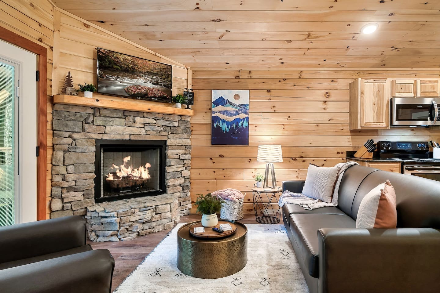 Cozy living room featuring a stone fireplace, leather sofa, and wooden walls with decorative artwork.