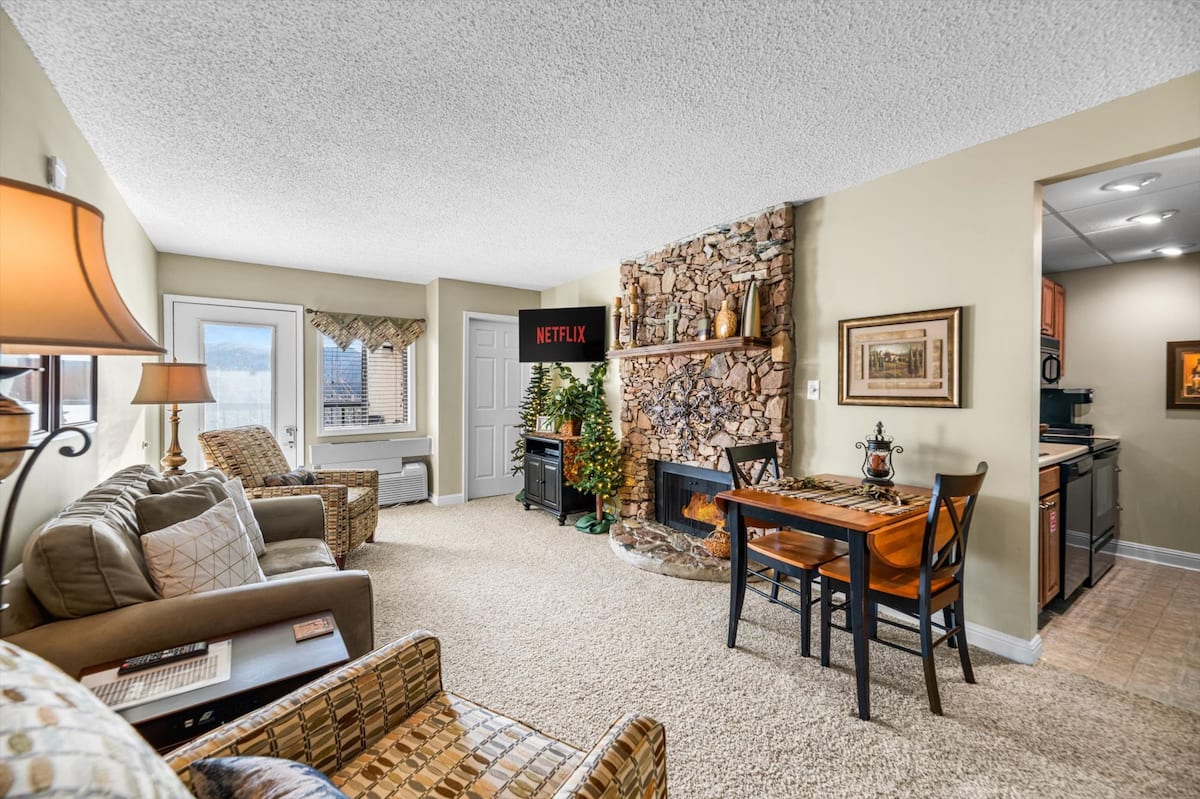 Cozy living room featuring a stone fireplace, a dining table, and a Netflix screen, with comfortable seating and warm decor.