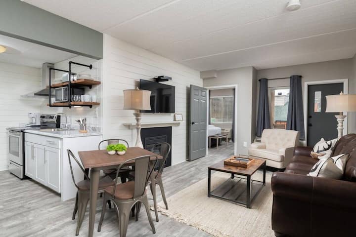 Cozy and modern interior of a living room and dining area with a small kitchen, featuring a sofa, dining table, and a TV.