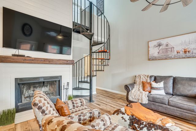 A cozy living room featuring a spiral staircase, a large flat-screen TV mounted on the wall, a stone fireplace, and comfortable seating arranged around a wooden coffee table.