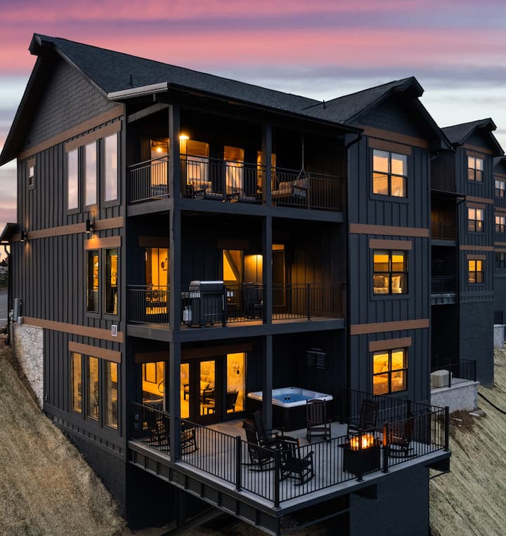 Exterior view of a modern cabin with multiple levels, featuring large windows and balconies, set against a sunset sky.