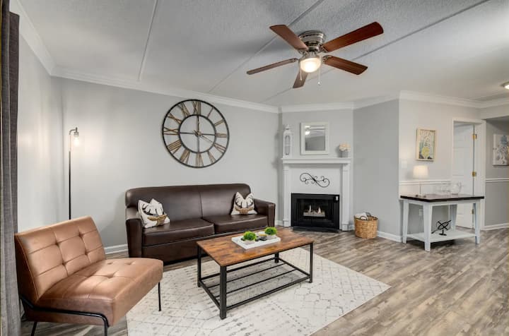 Cozy living room with a brown leather sofa, a wooden coffee table with decorative items, and a stylish clock on the wall.