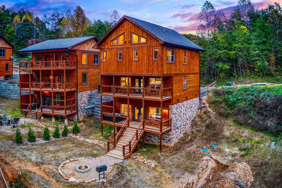 A picturesque vacation cabin with multiple levels featuring wooden siding, balconies, and outdoor seating, surrounded by trees and a fire pit area.