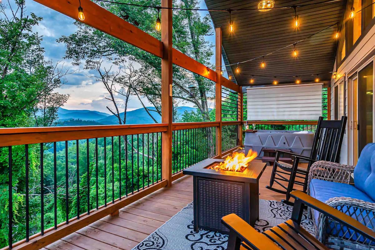 View of a scenic balcony featuring a fire pit, rocking chairs, and mountain landscape in the background.