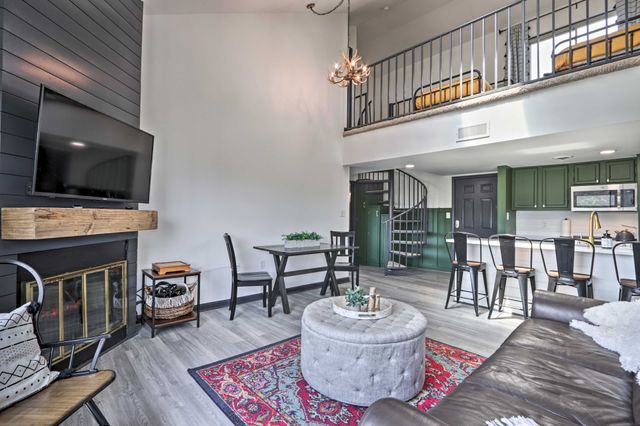 Modern living room with a cozy fireplace, a round ottoman, a sectional sofa, and a spiral staircase leading to a loft area.