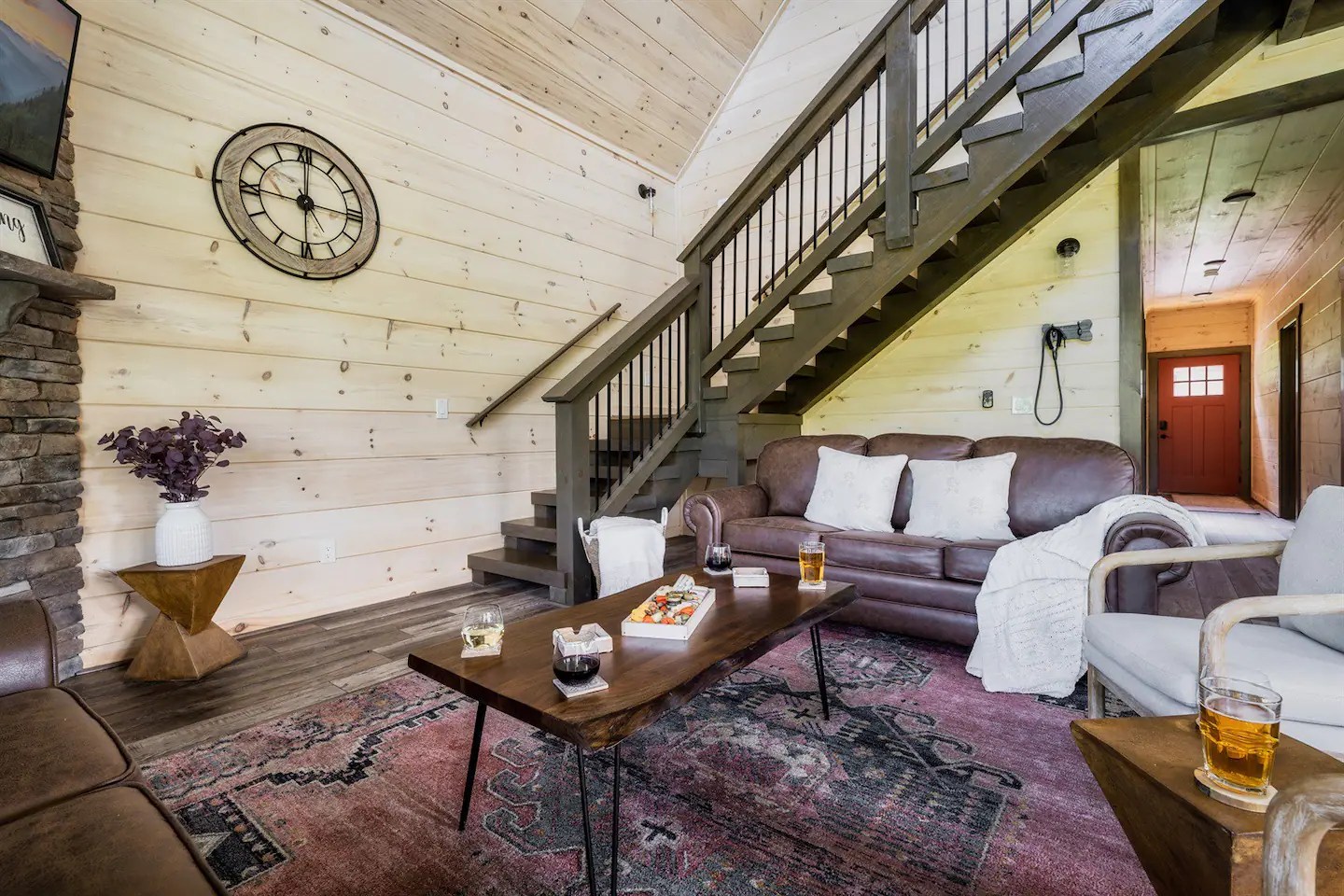 Cozy living area with a brown leather sofa, wooden coffee table, and decorative rug, featuring a clock on the wall and a staircase leading to an upper level.