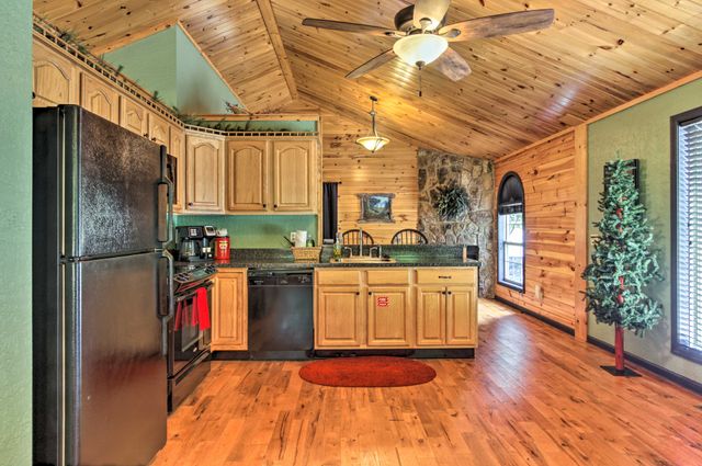 Interior view of a cozy cabin kitchen featuring wooden cabinets, a black refrigerator, and a dishwasher, with a wooden ceiling and rustic decor.