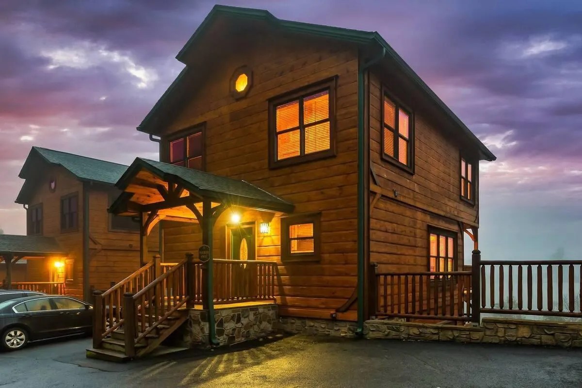 A cozy wooden cabin with warm lights glowing from the windows, set against a vibrant sunset sky.