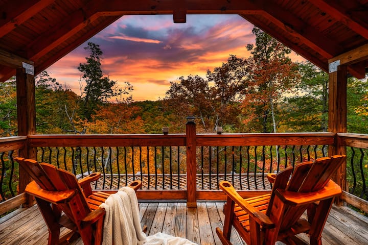 A cozy balcony view with two wooden rocking chairs overlooking vibrant autumn trees and a colorful sunset sky.